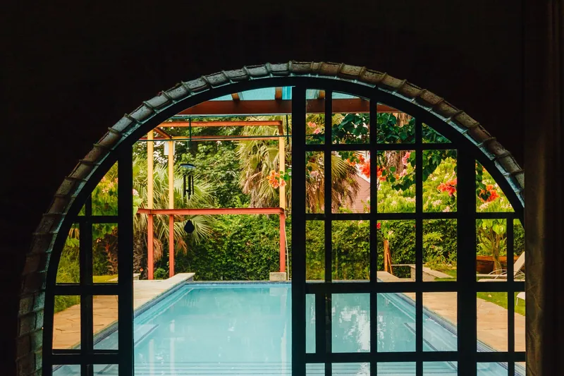 Arched glass doors opening onto a pool and tropical garden